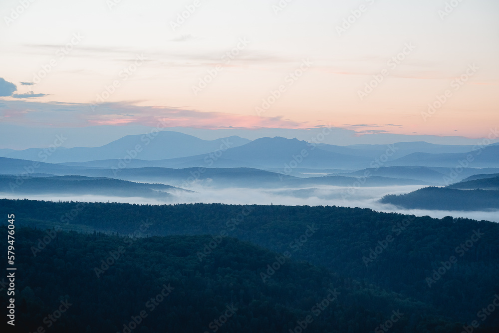 Morning fog filled the lowlands in the river valley, the mountains are visible in the distance, the taiga at dawn of the day, the bluish perspective.