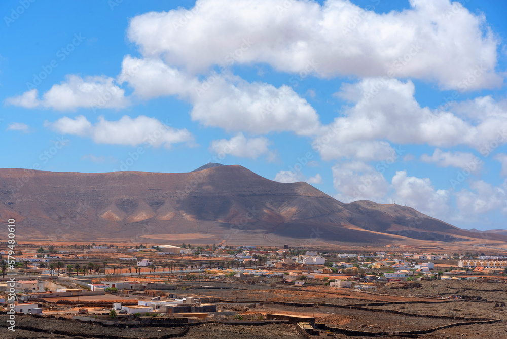 vista panorámica de un paisaje desértico y volcánico con el pueblo La Oliva con pequeñas casas blancas en el fondo una gran montaña volcánica en un día soleado y claro Fuerteventura islas canarias