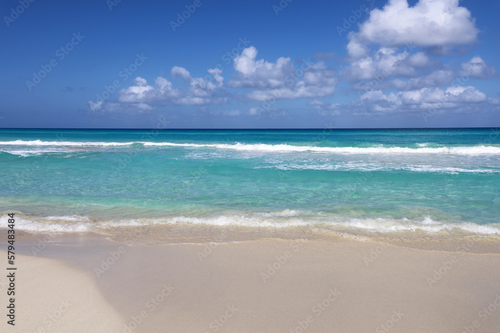 Tropical beach with white sand on a ocean, view to azure waves and sky with clouds. Caribbean coast, Background for holidays on a paradise nature