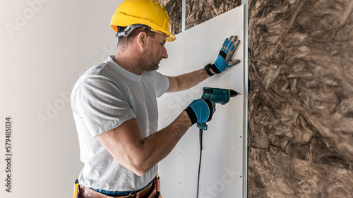 An electric quick screwdriver in the hand of a plasterer is screwing the plasterboard to the metal frame. photo