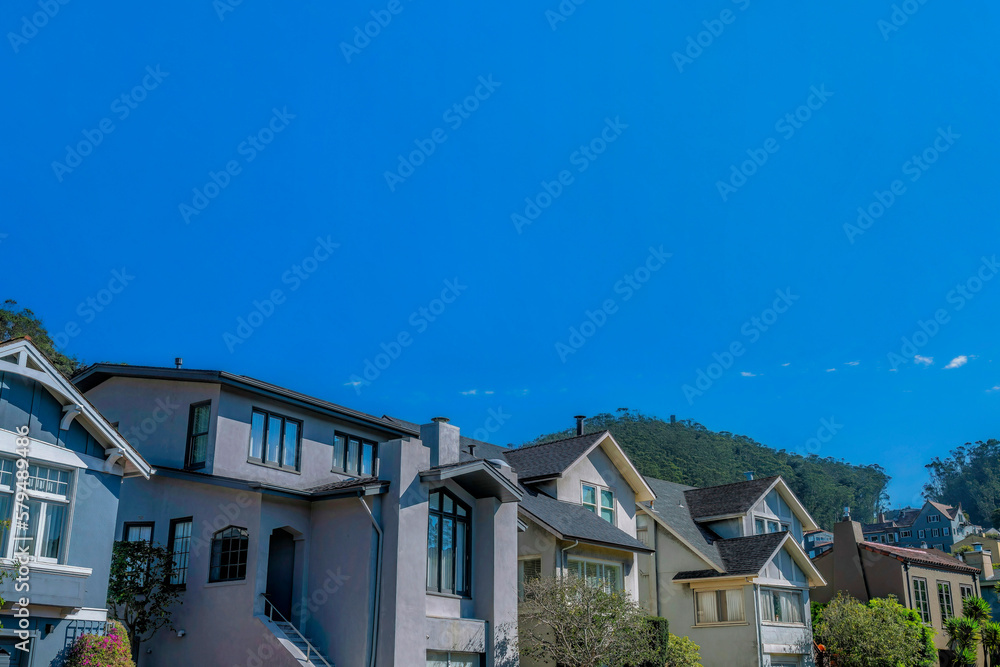 Street view of houses against blue sky in San Francisco California neighborhood. Real estate landscape with homes featuring gray walls lit by sunlight on a sunny day.