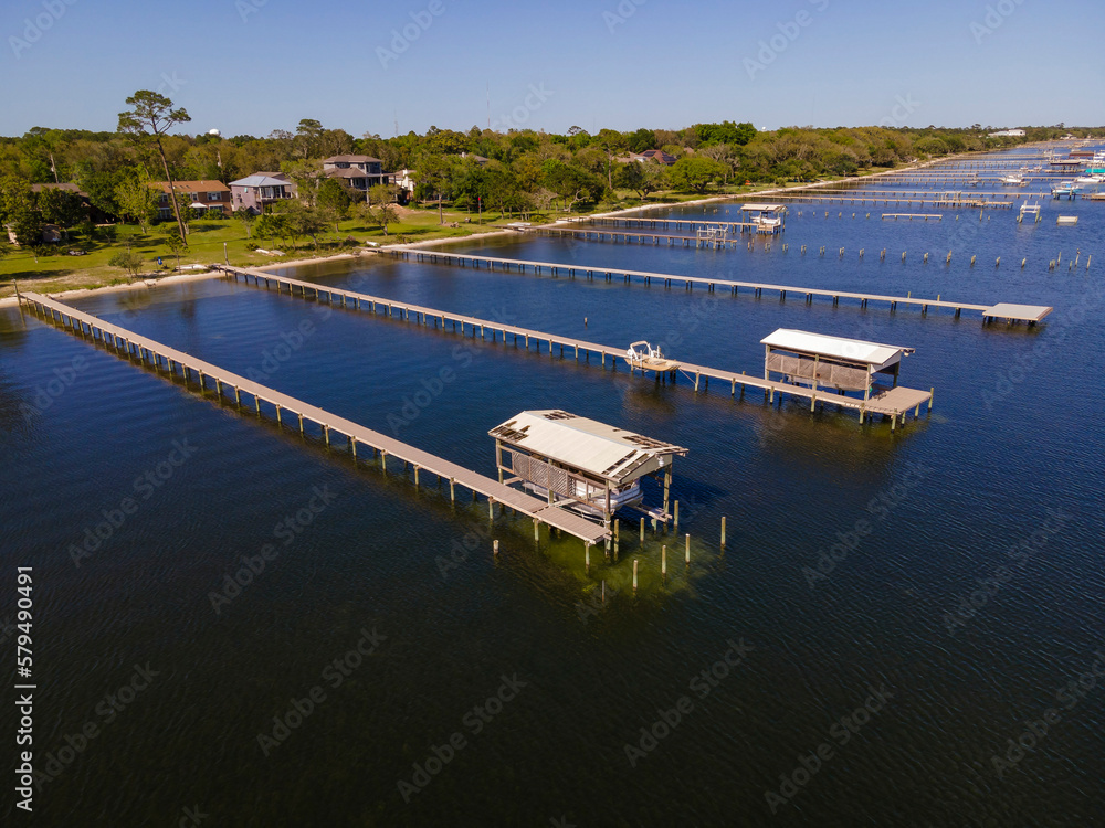 Fototapeta premium Villas on a neighborhood at Navarre, Florida with private docks with boat lifts at waterfront. High angle view of house waterfront with tall trees outdoors.