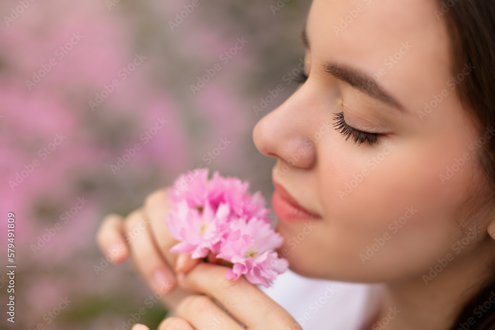 Young woman romantic close up portret in a blooming sakura garden. Wind is hairs. Spring story. Brown-haired girl smiles with a flower in her hairs closing her eyes and enjoy of spring mood Young woman romantic close up portret in a blooming sakura garden. Wind is hairs. Spring story. Brown-haired girl smiles with a flower in her hairs closing her eyes and enjoy of spring mood