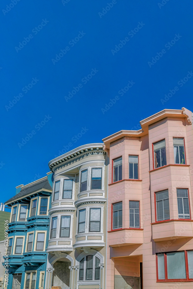 Homes with vibrant colorful walls against blue sky in San Francisco California. Residential landscape of houses with bay windows and flat roof tops viewed on a sunny day.