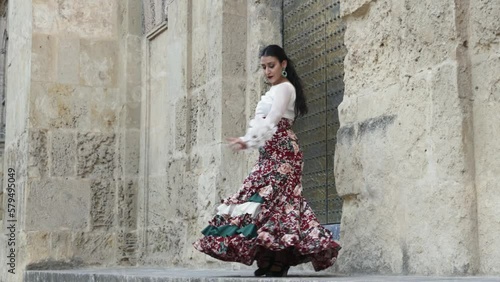 Hispanic gypsy woman flamenco dancer dressed in typical flamenco dress with red flowered skirt and white shirt dancing next to a wall of an old building