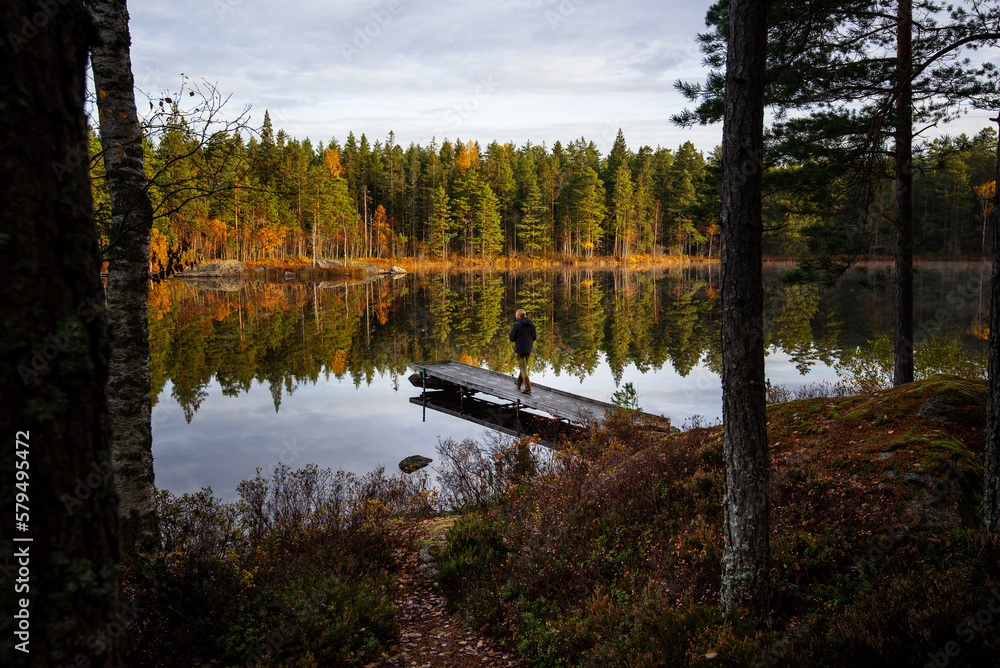 Fisherman walking out on foot bridge in calm forest lake with fall colors in the trees