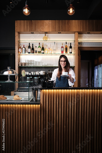A friendly waitress giving cup of coffee to a customer while standing behind a bar counter.