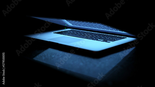 Laptop on a black background. Slightly open laptop. The computer screen lights up, the keyboard lights up