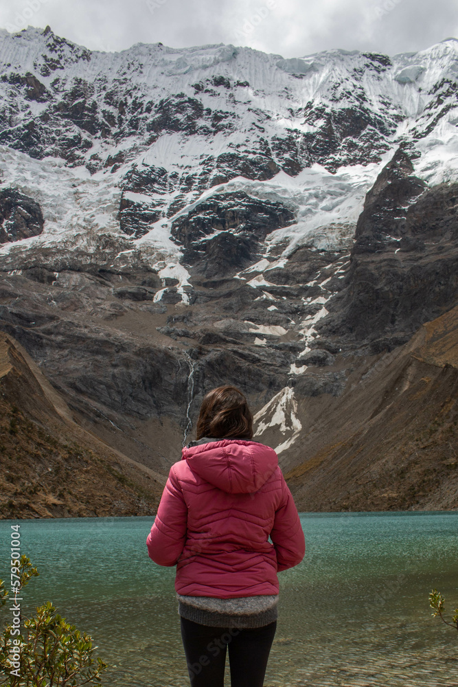 young woman standing on her back in front of the Humantay lagoon in Peru, glacial lake with turquoise waters. 