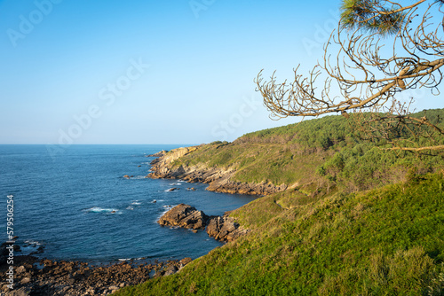 Beautiful scenic view of the natural rocky coast of Hondarribia in a blue sky day with forest and mountain by the Cantabrian sea, Hondarribia, Guipuzcoa, Basque Country, Spain photo
