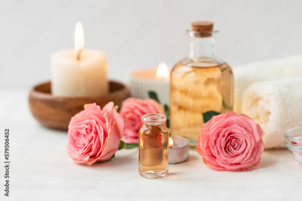 Aromatherapy. Concept of pure organic essential rose oil. Elixir with plant based floral or herbal ingredients. Pink flowers extract. Spa atmosphere with candle, towel. White background Aromatherapy. Concept of pure organic essential rose oil. Elixir with plant based floral or herbal ingredients. Pink flowers extract. Spa atmosphere with candle, towel. White background