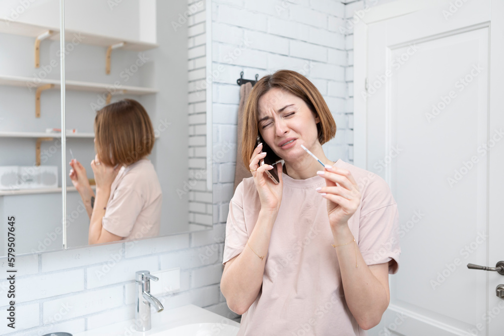 Young excited woman standing in the bathroom, talking on mobile phone and telling to her husband about positive result of pregnancy test Young excited woman standing in the bathroom, talking on mobile phone and telling to her husband about positive result of pregnancy test