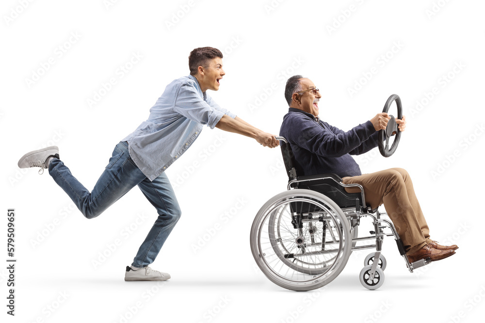 Full length profile shot of a guy pushing a mature man in a wheelchair holding a steering wheel Full length profile shot of a guy pushing a mature man in a wheelchair holding a steering wheel