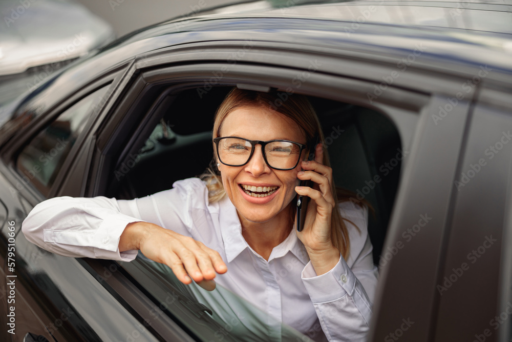 Smiling businesswoman traveling on back seat of car and talking smartphone while looking at window Smiling businesswoman traveling on back seat of car and talking smartphone while looking at window
