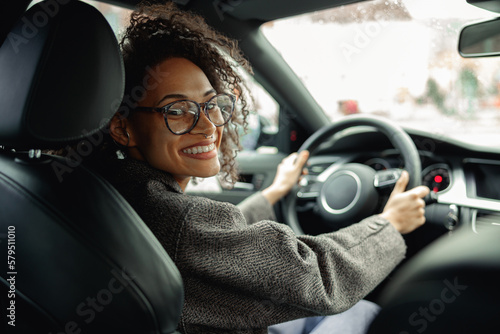 Tableau sur toile Smiling woman manager driving car and holding both hands on steering wheel on th