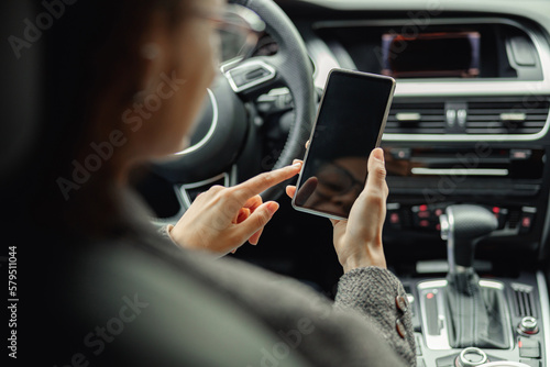 Close up of businesswoman hands is using phone while sitting behind steering wheel in own car