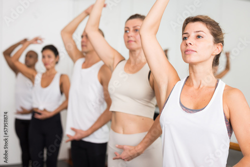 Group of people doing exercises using barre in gym with focus to fit athletic toned ..woman in foreground in health and fitness concept