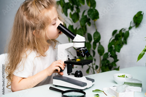 a little blonde girl at a table studying plants with a magnifying glass and a microscope  the concept of ecology and biology  earth day