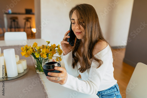Attractive European stylish woman with dark wavy hairstyle in white shirt and jeans sitting with coffee and smartphone in the morning in sunny day 