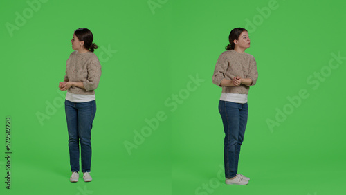 Young adult doing advertisement and example sign on camera, standing over full body green screen backdrop. Casual relaxed woman showing presentation icon and advertising something in studio.