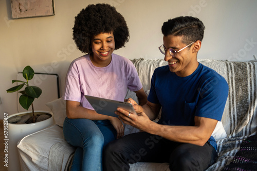 Happy Latin couple using digital tablet on sofa indoors