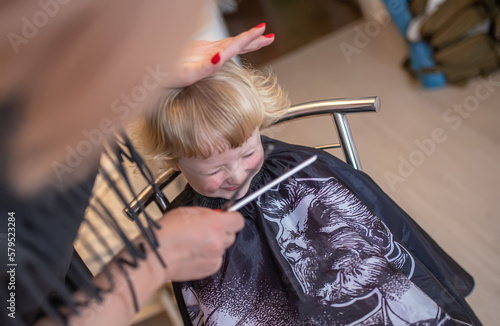 The little girl squinted her eyes on the hairdresser's chair. combing a girl's hair in a hairdressing beauty salon.
