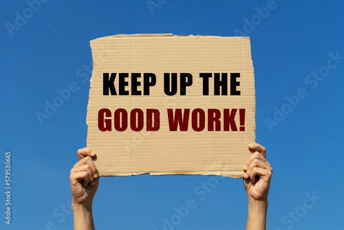 Keeo up the good work text on box paper held by 2 hands with isolated blue sky background. This message board can be used as business concept to continue good performance.