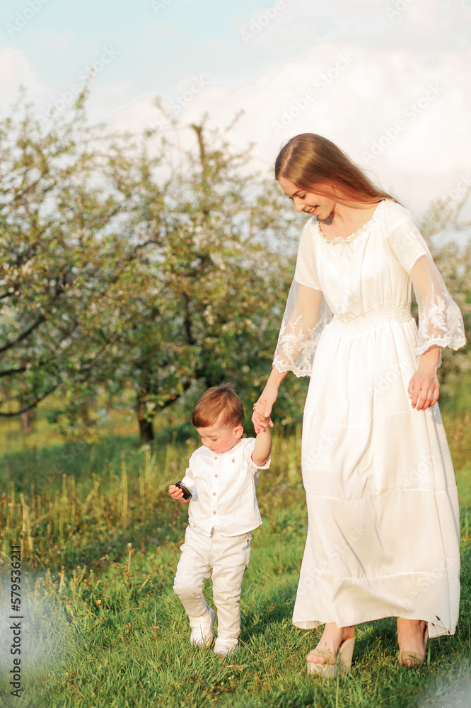 Fototapeta premium Portrait of happy mother and her baby boy. Beautiful touching scene of mom and son. Blooming garden in spring.