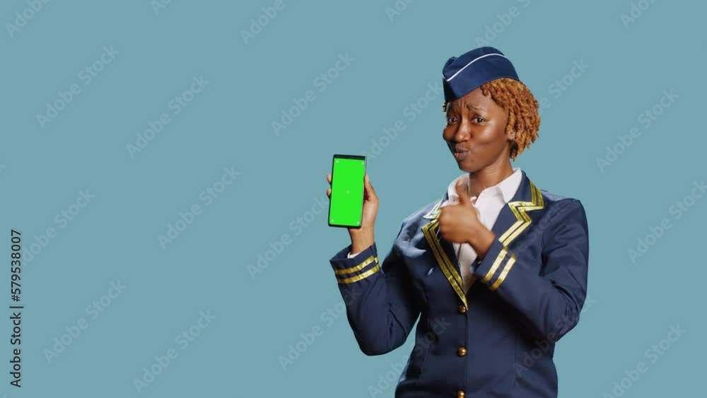 African american woman holding phone with greenscreen, showing isolated display with blank copyspace in studio. Female airliner looking at mockup template on screen over blue background. African american woman holding phone with greenscreen, showing isolated display with blank copyspace in studio. Female airliner looking at mockup template on screen over blue background.