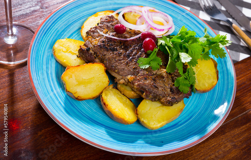Tasty beef steak with baked potatoes and sauce at plate with greens