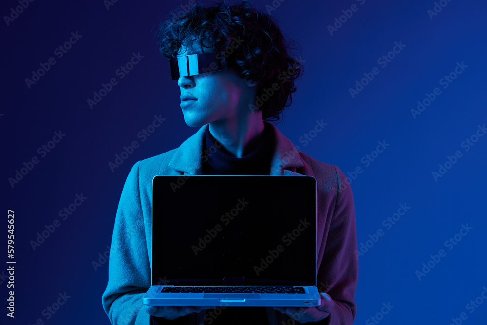 Portrait of a stylish male hacker with a laptop and futuristic glasses in blue light, Blue Perennial color, cyber security, technology, open laptop copy space, template Portrait of a stylish male hacker with a laptop and futuristic glasses in blue light, Blue Perennial color, cyber security, technology, open laptop copy space, template