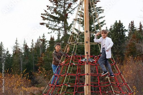 A boy and a girl are climbing the net in the outdoor playground in fall.