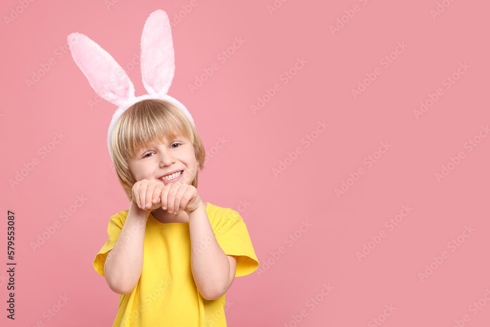 Happy boy wearing bunny ears headband on pink background, space for text. Easter celebration