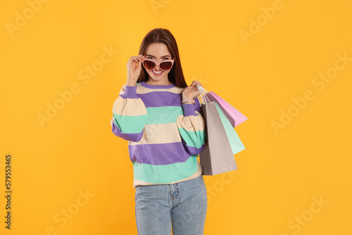 Happy young woman with shopping bags on yellow background. Big sale