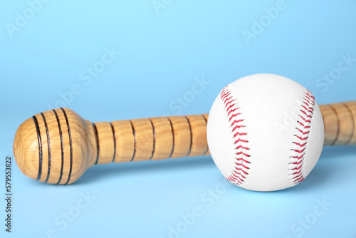 Wooden baseball bat and ball on light blue background, closeup. Sports equipment