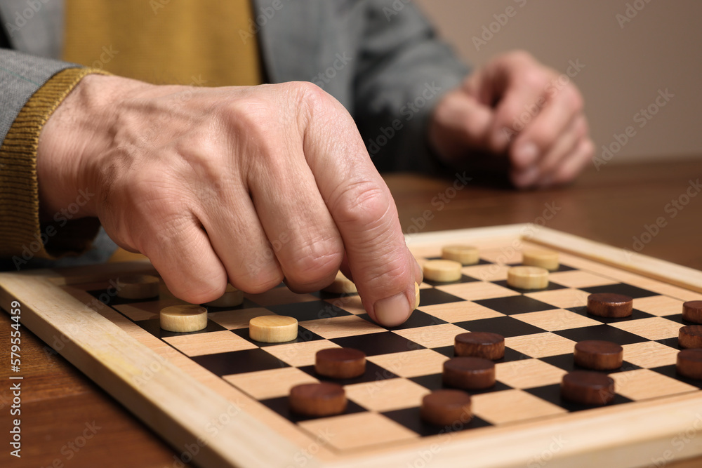 Playing checkers. Senior man thinking about next move at wooden table, closeup Playing checkers. Senior man thinking about next move at wooden table, closeup