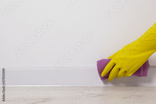 Woman in protective glove cleaning plinth with washcloth indoors, closeup. Space for text