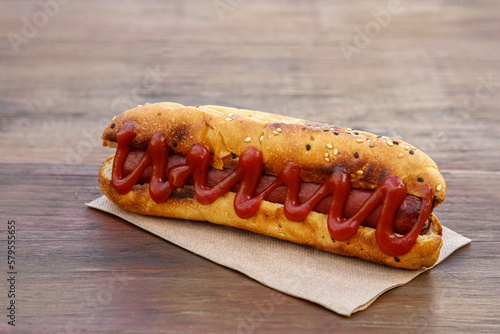 Fresh tasty hot dog with ketchup on wooden table, closeup