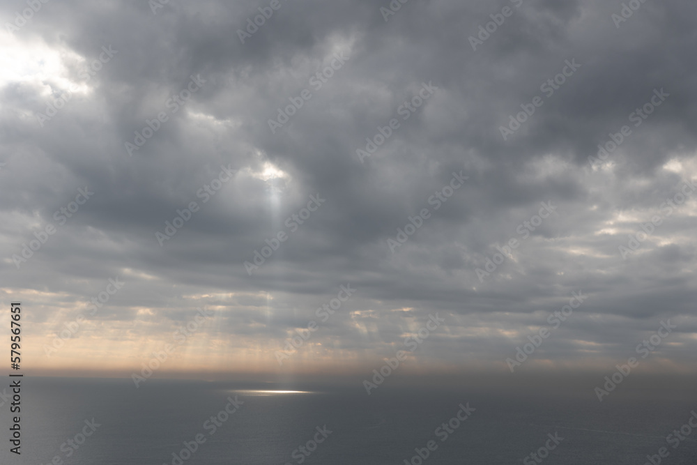 The sun rays breaking through gray clouds reflecting on the sea surface