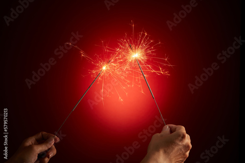 Front view of burning sparks close up in hand, pyrotechnics, shining fire flame on dark background. Happy new year and merry christmas concept. Advertising photo.