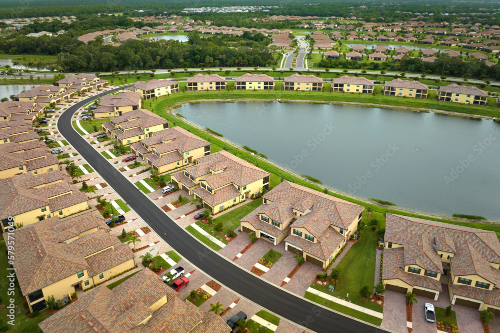 Aerial view of tightly packed homes in Florida closed living clubs with lake water in the middle. Family houses as example of real estate development in american suburbs