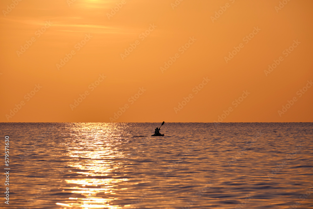 Dark silhouette of lonely fisherman rowing on his boat on sea water at sunset