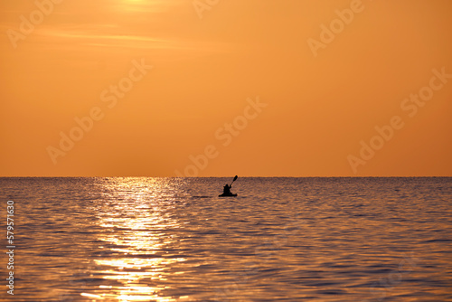 Dark silhouette of lonely fisherman rowing on his boat on sea water at sunset © bilanol