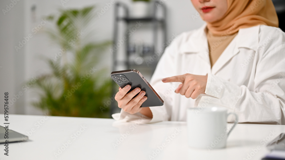 Cropped image of attractive Asian Muslim businesswoman using her phone at her desk. Cropped image of attractive Asian Muslim businesswoman using her phone at her desk.