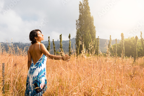 As the sun beats down on a peaceful rural landscape, a joyful Latina woman frolics in the golden fields