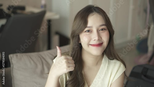 smile asian women sit on sofa in livingroom looking camera thumb up