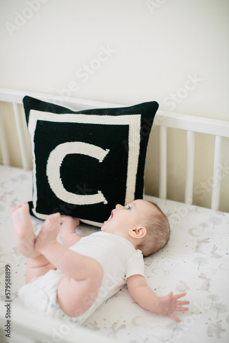 baby girl lying in crib with black and white letter 'c' pillow next to her  photo