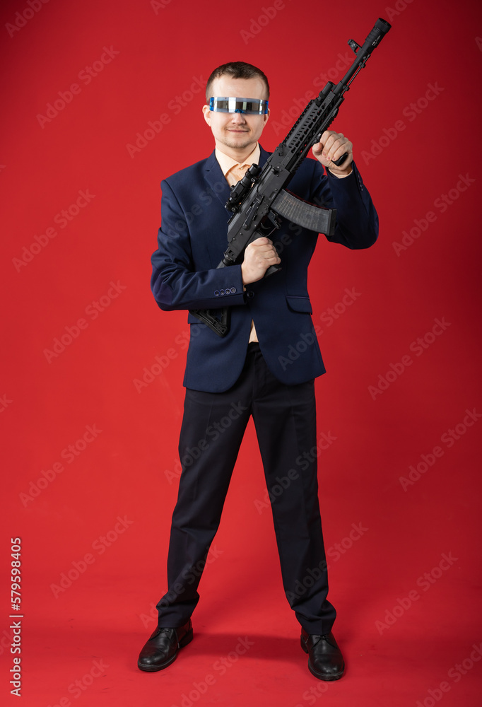 businessman with a gun. a guy in fashionable glasses, a suit holds a machine gun. Business concept. red background businessman with a gun. a guy in fashionable glasses, a suit holds a machine gun. Business concept. red background