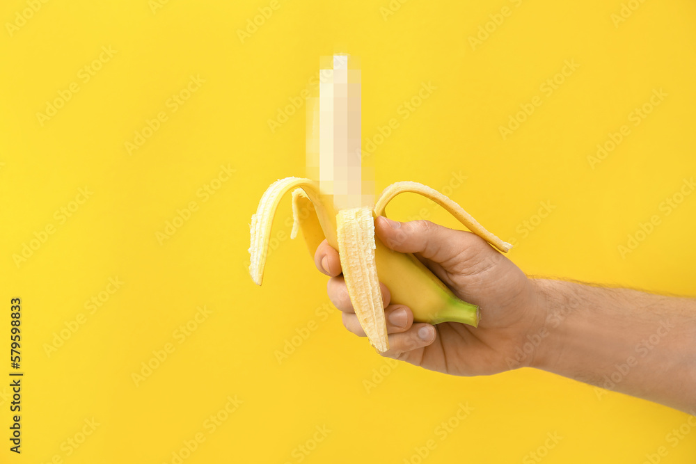 Male hand with banana on yellow background. Concept of sex education - obrazy, fototapety, plakaty 