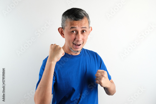 Portrait of a satisfied Asian man with casual tshirt celebrating success isolated over white background.
